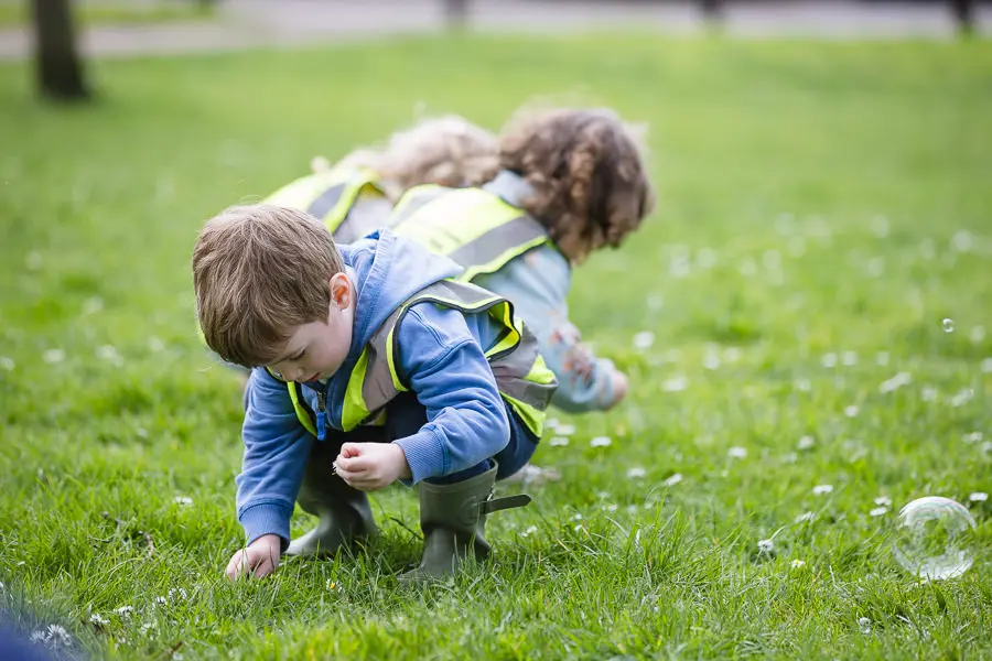 Three children with hi-vis vests on playing in the grass